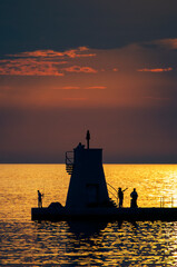 Fototapeta premium People on pier with small lighthouse at sunset