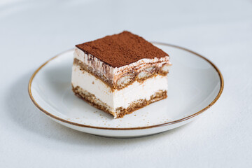 Tiramisu cake dessert served with coffee, biscuit and cocoa as ingredients on a bright white background. One piece of cake