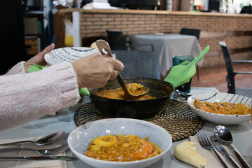 Woman serving a soupy rice with a saucepan. A highly demanded food in Spain 