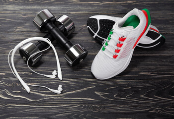 Sports training shoes, dumbbells, headphones on a dark wooden background.