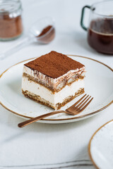 Tiramisu cake dessert served with coffee, biscuit and cocoa as ingredients on a bright white background. One piece of cake