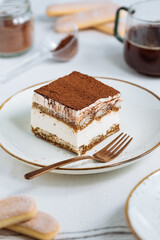 Tiramisu cake dessert served with coffee, biscuit and cocoa as ingredients on a bright white background. One piece of cake