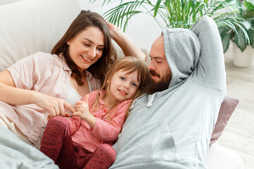 Happy family Mother father and daughter lie in bed rest hugging and having fun Play Tickle....