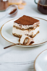 Tiramisu cake dessert served with coffee, biscuit and cocoa as ingredients on a bright white background. One piece of cake