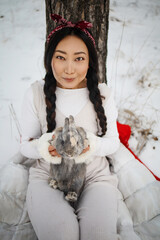 Asian girl holding a rabbit in her arms in a snowy forest. Friendship with the Easter bunny.
