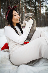Asian girl holding a rabbit in her arms in a snowy forest. Friendship with the Easter bunny.