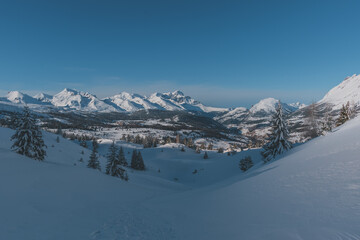 A picturesque landscape view of the snowcapped French Alps mountains with a hiking path and footprints in the snow on a cold winter day (Hautes-Alpes, Devoluy)