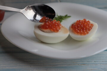 Put a spoonful of red caviar on boiled eggs, on a white plate.