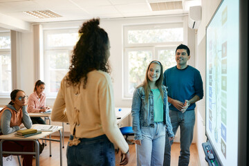 High school students and their teacher talking while using smartboard in the classroom.