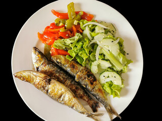 Isolated view of plated food, healthy fish meal, typical dish of Portuguese regional cuisine with grilled sardines with salad: red peppers, green peppers, sesame seeds, lettuce, onion and cucumber