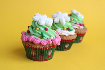 A cupcake with a lot of cream and decorated with a snowflake stands on a yellow background.