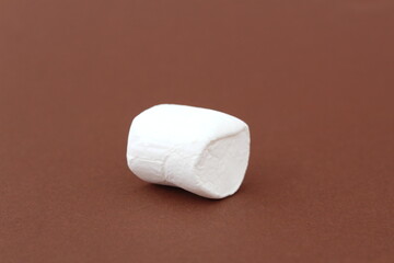 One white marshmallow lies on a brown background.
