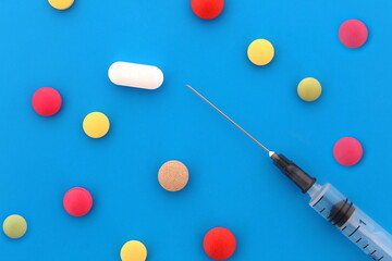 Loose pills and a syringe lie on a blue background.