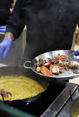 cocinero guisando una arroz caldoso de marisco con paelleras y trozos de bogavante