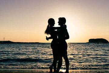 Photoshoot of young helthy beautiful couple, boy and girl, dating at the beach - Man and woman lovers dancing near the ocean in a sunny day looking at each others
