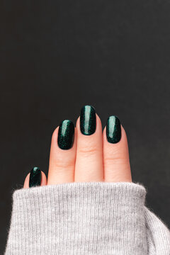 Female hand in gray knitted sweater with beautiful manicure - green glittered nails against gray background. Nail care concept
