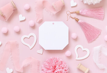 Fototapeta na wymiar Blank gift tag, hearts, flowers, silk ribbons and tassel earrings on pink top view, label mockup