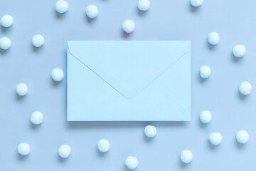 Blank envelope near pastel pom-poms on light blue top view