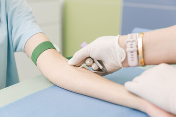 Obraz premium Taking a blood test from a vein in the treatment room. Nurse pricking a syringe with a needle into the patient hand. Swab pressed against the injection site during blood donation. Tube with blood