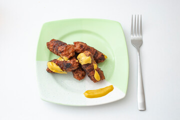 Romanian , traditional meat rolls, called ”mici” or ”mititei” with mustard   on a green ceramic plate, isolated on white