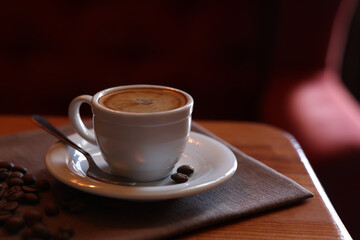 Cup of hot aromatic coffee and roasted beans on wooden table in cafe. Space for text