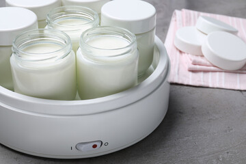 Modern yogurt maker with full jars on grey table, closeup