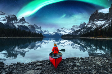Traveler woman sitting on canoe with aurora borealis over Spirit Island in Maligne lake at Jasper...