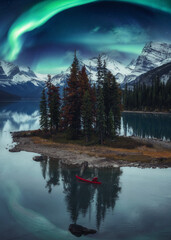 Traveler man canoeing on Spirit Island with aurora borealis over rocky mountains in the night at...