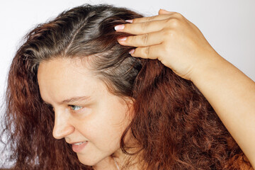 Naklejka premium Woman showing graying hair roots by pushing left side of hair back on white background. Regrown roots which are in need of recoloring. Anti age care. Copy space.