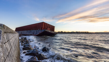 Barge container ship collided on a rocky coast during wind storm. Sunset Sky. Seawall, Downtown Vancouver, British Columbia, Canada.