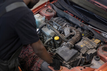 Part of young automechanic in workwear checking engine of car while standing by open hood with motor