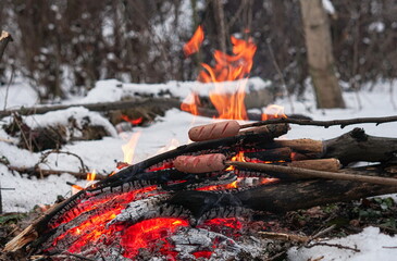 Sausages on the stick grilled in the fire. Winter forest.