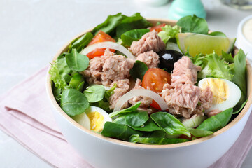 Bowl of delicious salad with canned tuna and vegetables on light table, closeup