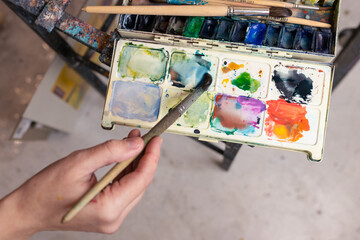 Close-up of the artist's hand with a brush and multicolored watercolor paints