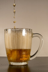 The glass is filled with beer and foam, beer pours into the glass. Transparent glass with light beer and thick foam.