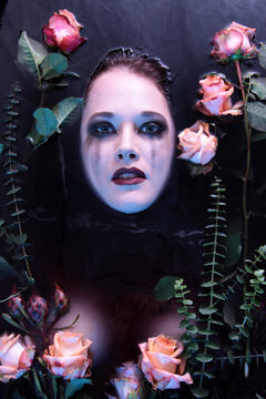 Eine Frau versinkt in dunklem Wasser mit Rosen umgeben