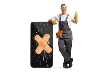 Full length portrait of a repairman leaning on a broken smartphone with bandage and showing thumbs...