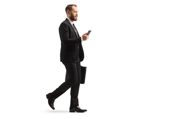 Full length profile shot of a young businessman walking and using a mobile phone with a briefcase in his hands