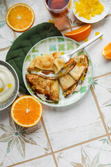 Orange pancakes with custard and candied fruits on a light plate. Pancake week, maslenitsa. Table setting in light style for lunch