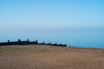 Wooden groyne water breakers on a pebble beach in Whitstable on a bright winter day with blue sky...