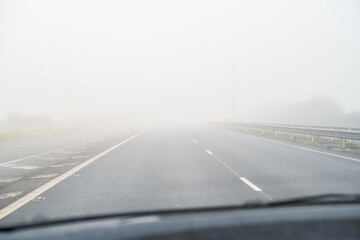 Fototapeta premium A misty, foggy road and dashed white centre line as seen through a car windscreen. There is slight motion blur.