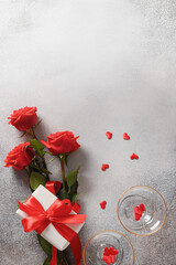 Valentine's day greeting card with gift, red roses, wine glasses on gray background. Vertical format with copy space.