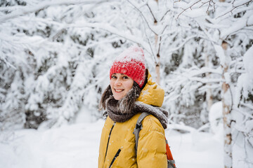 Fototapeta na wymiar A girl on the street smiles beautifully in winter. A young woman walks in the park in the cold season, snow falls, a beautiful winter forest. The girl laughs, looks straight.