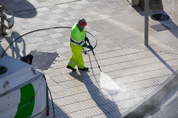Worker cleaning a sidewalk with high pressure water jet machine on sunny day