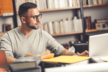 Male student studying in campus library.He reads a book.