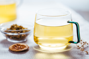 Cup of chamomile tea in transparent mug served with slice of lemon and orange. Tea break. 