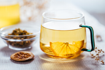Cup of chamomile tea in transparent mug served with slice of lemon and orange. Tea break. 
