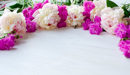 White peonies flowers with pink carnations on white wooden background with place for text