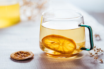Cup of chamomile tea in transparent mug served with slice of lemon and orange. Tea break. 