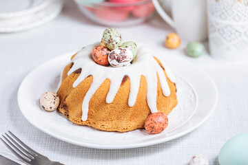 Easter cake with colorful eggs in a chocolate nest on pink background and flowers. Happy Easter concept. Dessert also known as  Kuglof. Top view